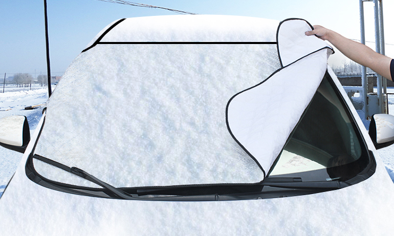 Windscreen frost cover fitted over a snow-covered car windscreen, being lifted off